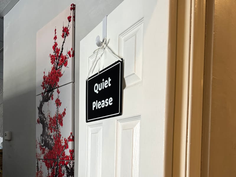 Quiet Please sign hanging on a white treatment-room door beside cherry-blossom art